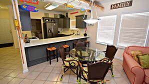 A kitchen with a dining area, a refrigerator, a sink, and a 'Happy Hour' sign. - Spinnaker Pointe (Gulf Shores)