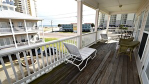A wooden deck with white railings, a lounge chair, and wicker chairs. - Spinnaker Pointe (Gulf Shores)