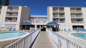 A pool area with a wooden deck, lounge chairs, and umbrellas. - Sugar Beach (Orange Beach)