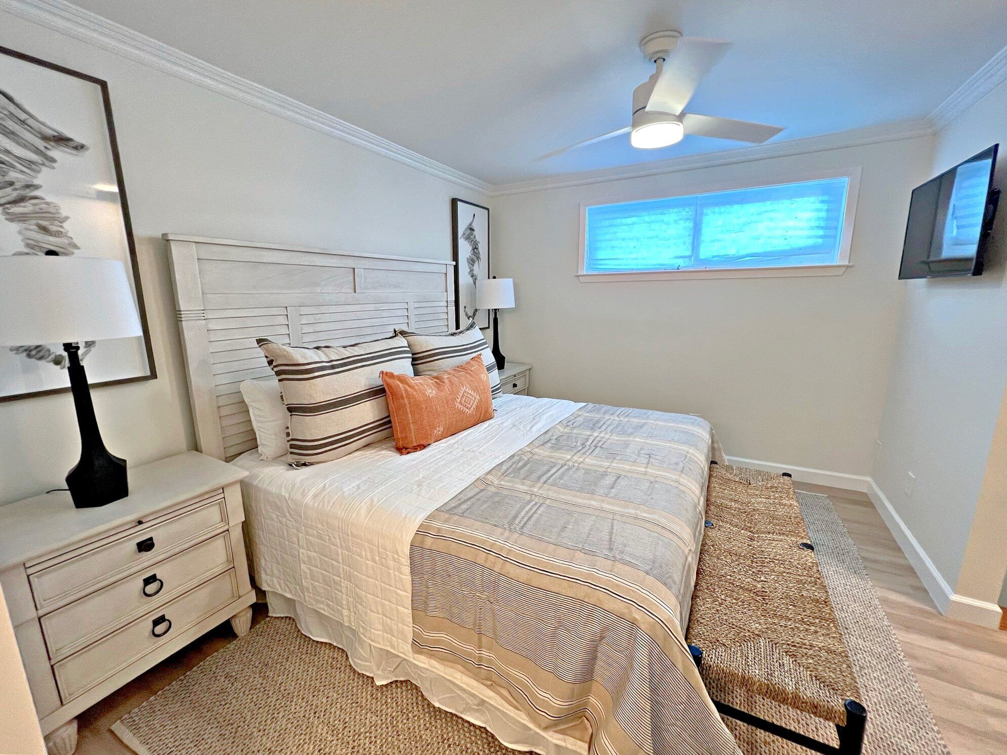 A bedroom with a bed, nightstands, a ceiling fan, a window, and a TV.