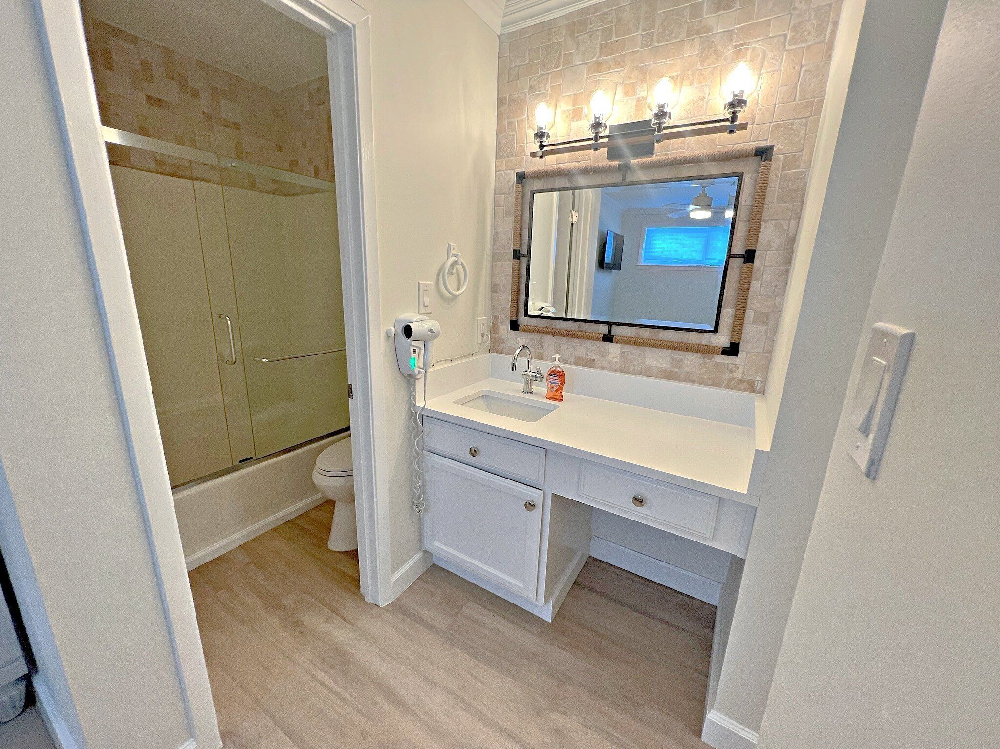 A bathroom with a white vanity, a mirror with lights, a shower, and a toilet.