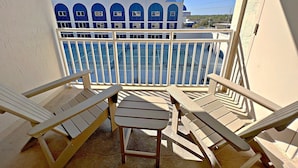 A balcony with two wooden chairs and a small table, overlooking a building with blue windows and a blue roof. - Sugar Beach (Orange Beach)