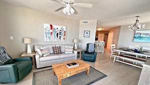 A modern living room with a sofa, coffee table, and a dining area with a table and chairs. - Summerhouse (Orange Beach)