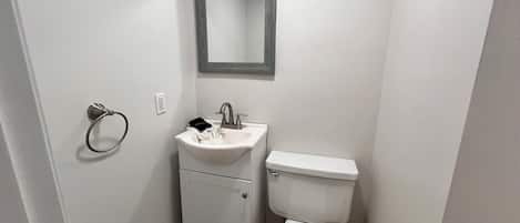 A small, white bathroom with a sink, mirror, and toilet.