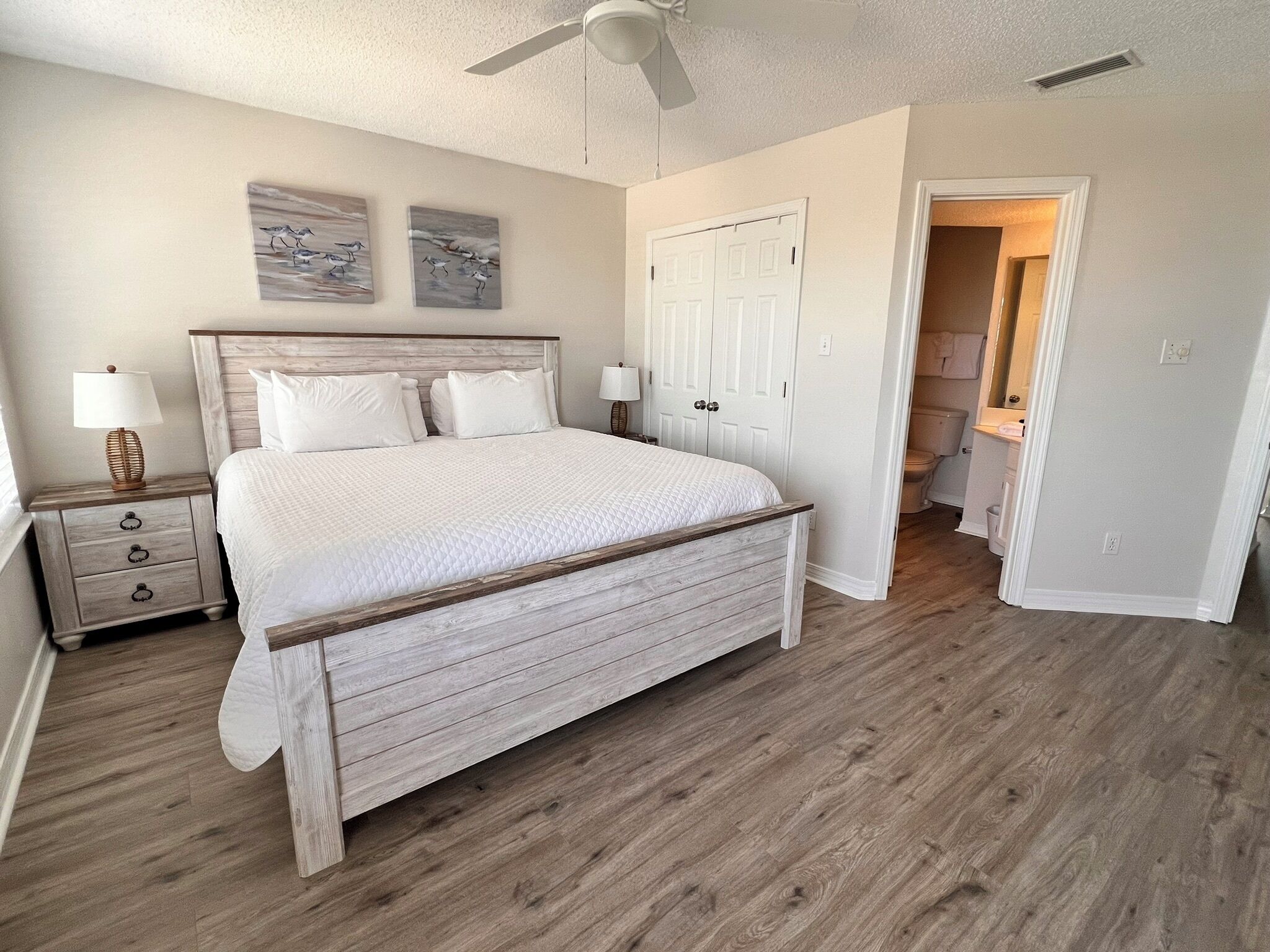 A bedroom with a wooden bed, a nightstand with a lamp, and a door leading to a bathroom.