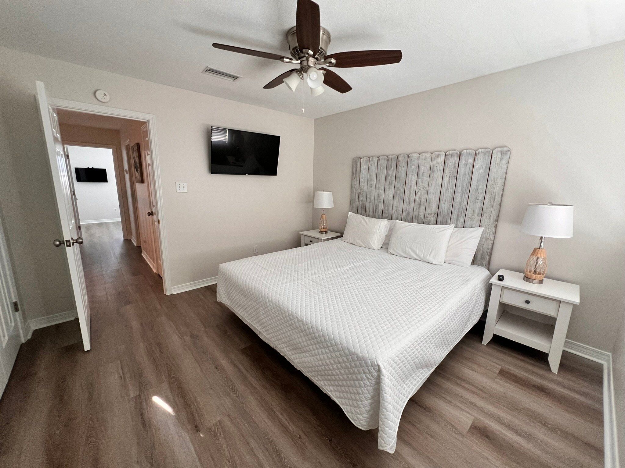 A bedroom with a large bed, a ceiling fan, a TV, and a nightstand with a lamp.
