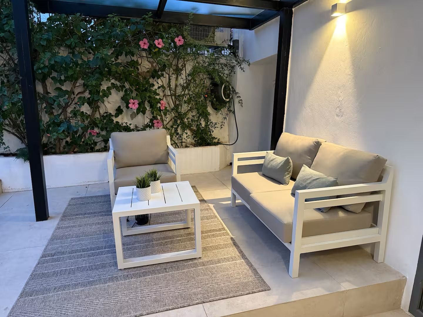 A covered outdoor seating area with a white sofa, a white coffee table, and a potted plant.