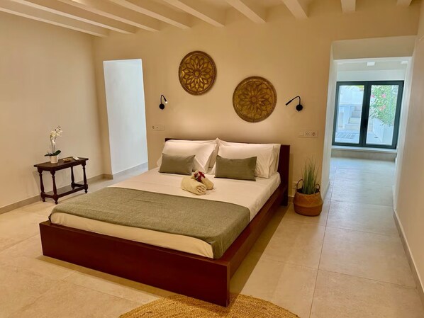 Un dormitorio con una cama grande, una mesita de noche con lámpara y una planta en maceta.