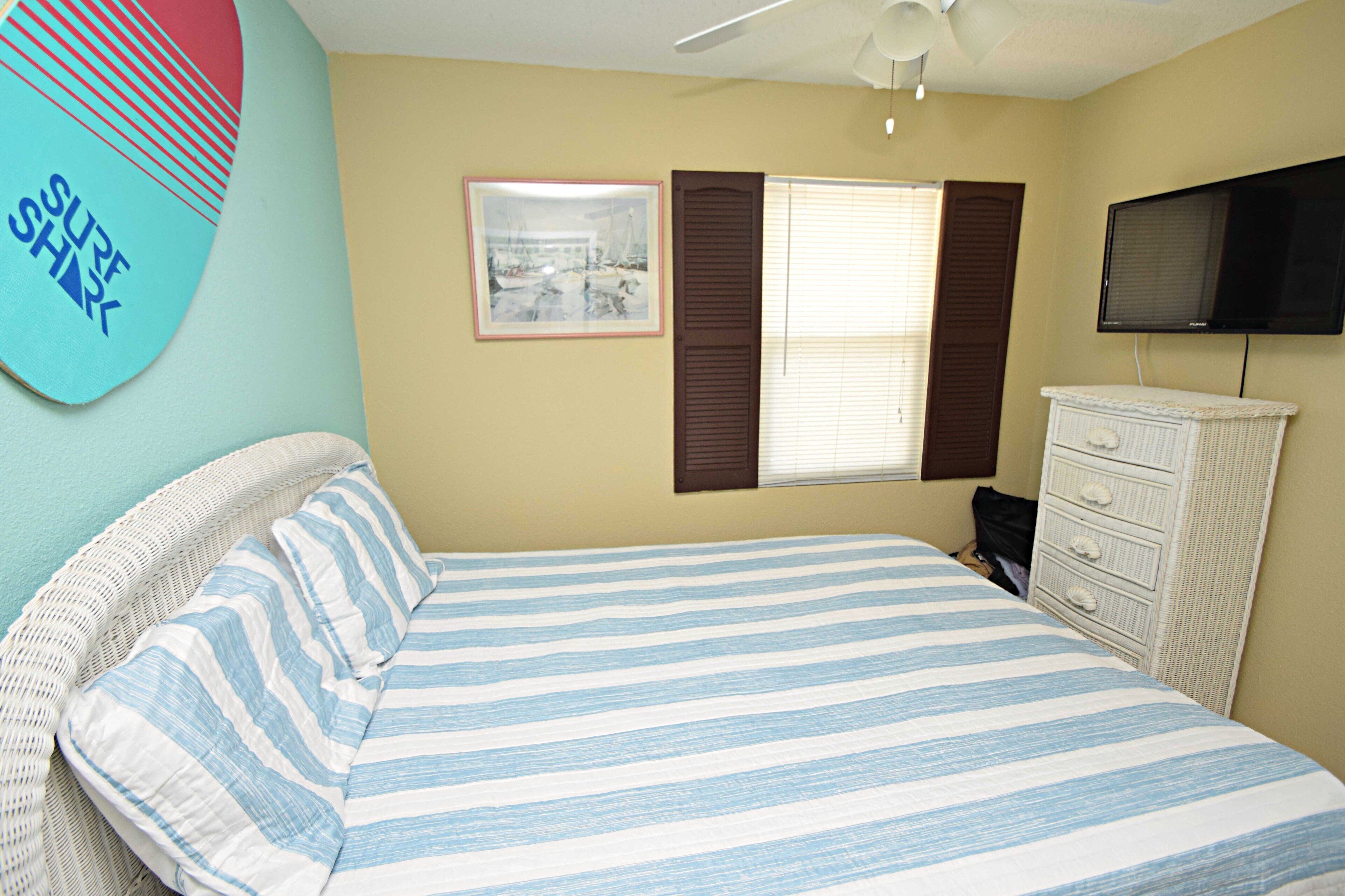 A bedroom with a bed, a dresser, a television, a window with blinds, and a wall decoration.