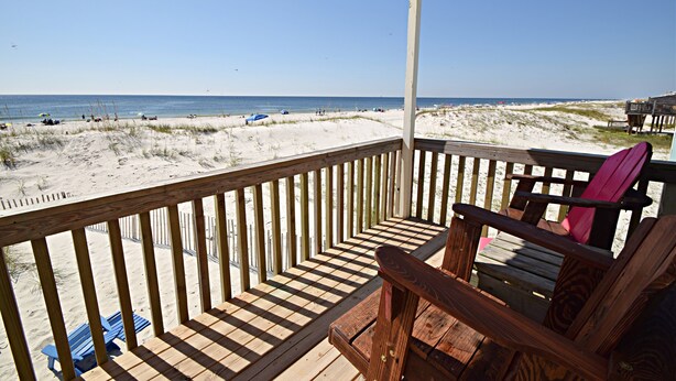 A wooden deck with a view of the beach, a wooden chair, and a blue lounge chair. - Sunrise Village (Gulf Shores)