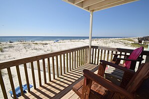 Une terrasse en bois avec vue sur la plage, une chaise en bois et un fauteuil de jardin bleu.