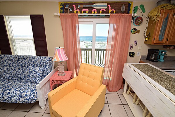 Une chambre avec vue sur la plage, un canapé, un fauteuil, une petite table avec une lampe et un coin cuisine.
