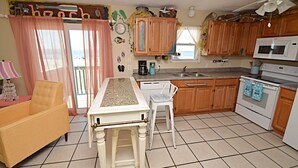 A kitchen with wooden cabinets, a white stove, a microwave, and a dining table with a chair. - Sunrise Village (Gulf Shores)