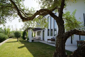 A modern house with a covered patio, a lawn, and a tree in the foreground. - Luxury Holiday Villa with private swimming pool amidst 300 olive trees (Ronda)
