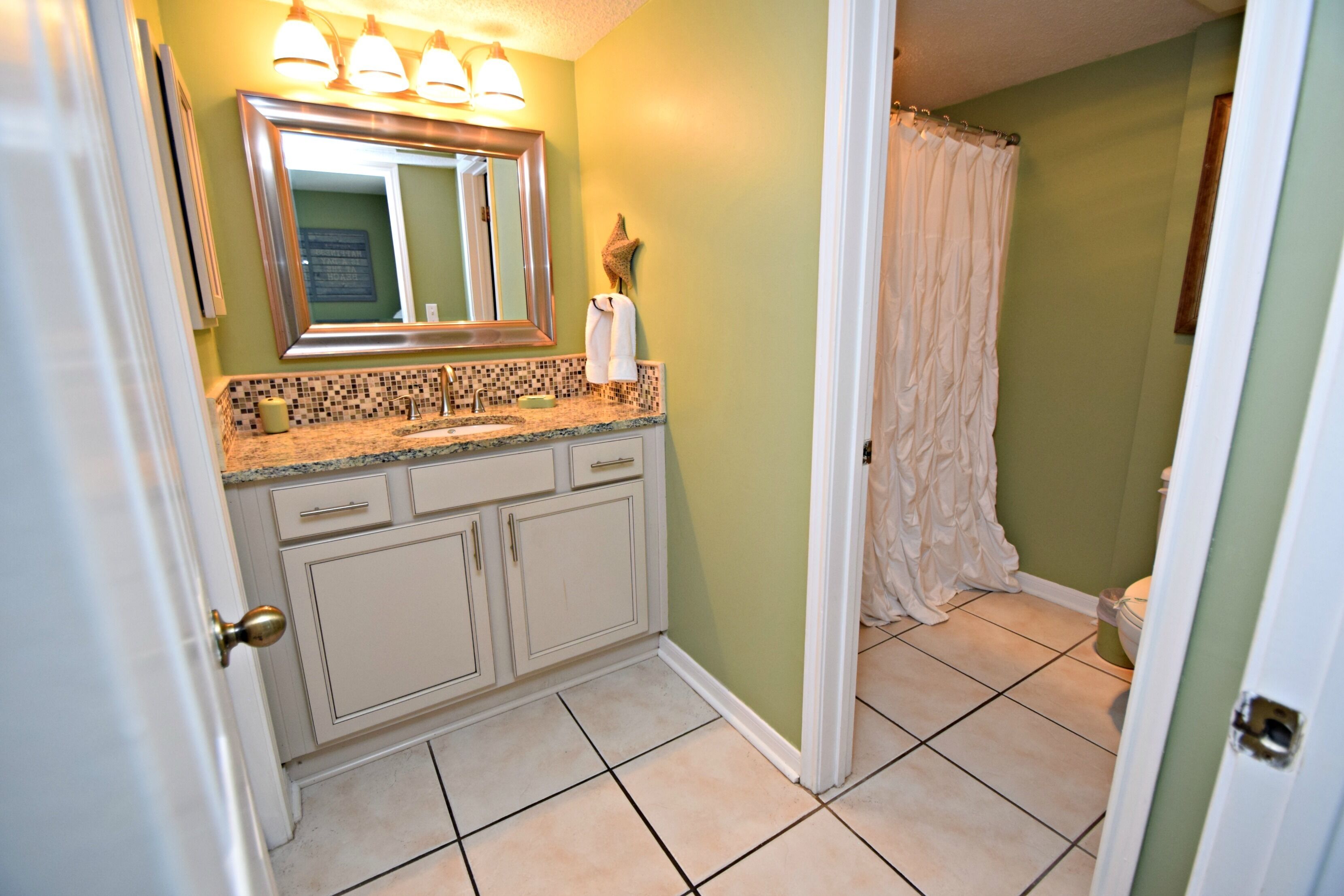 A bathroom with a tiled floor, a sink with a mirror above it, and a shower curtain.