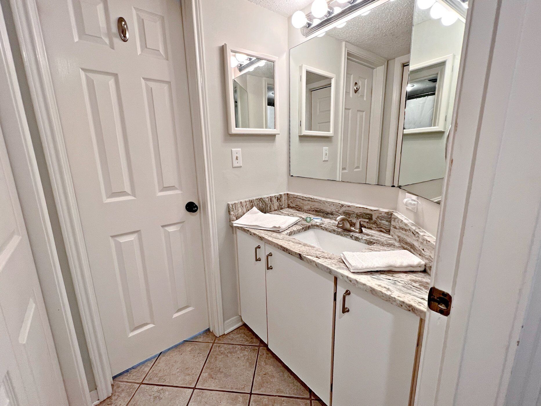 A bathroom with a white door, a sink with a marble countertop, and a mirror above the sink.