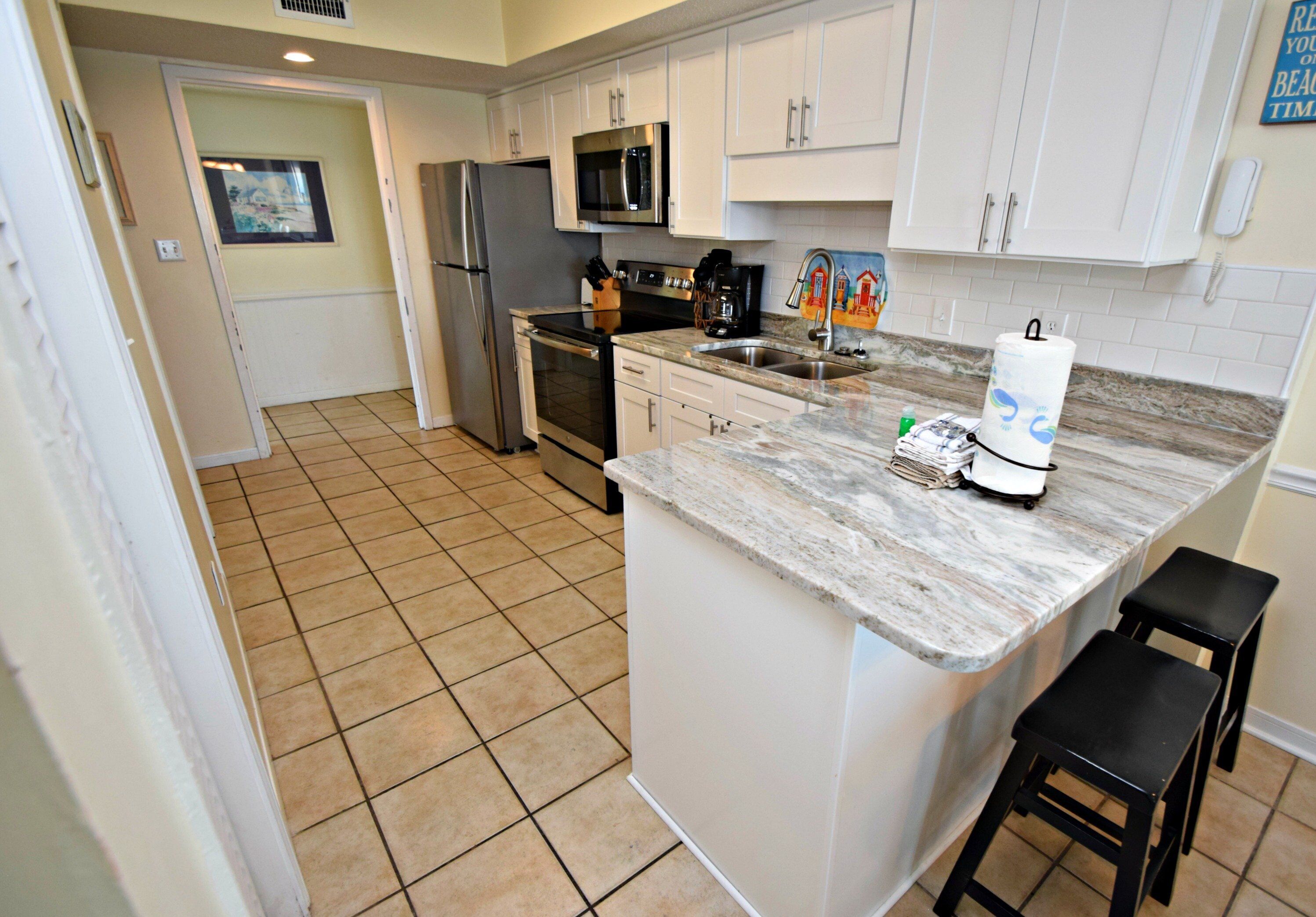 A kitchen with white cabinets, a stainless steel refrigerator, a microwave, and a sink.