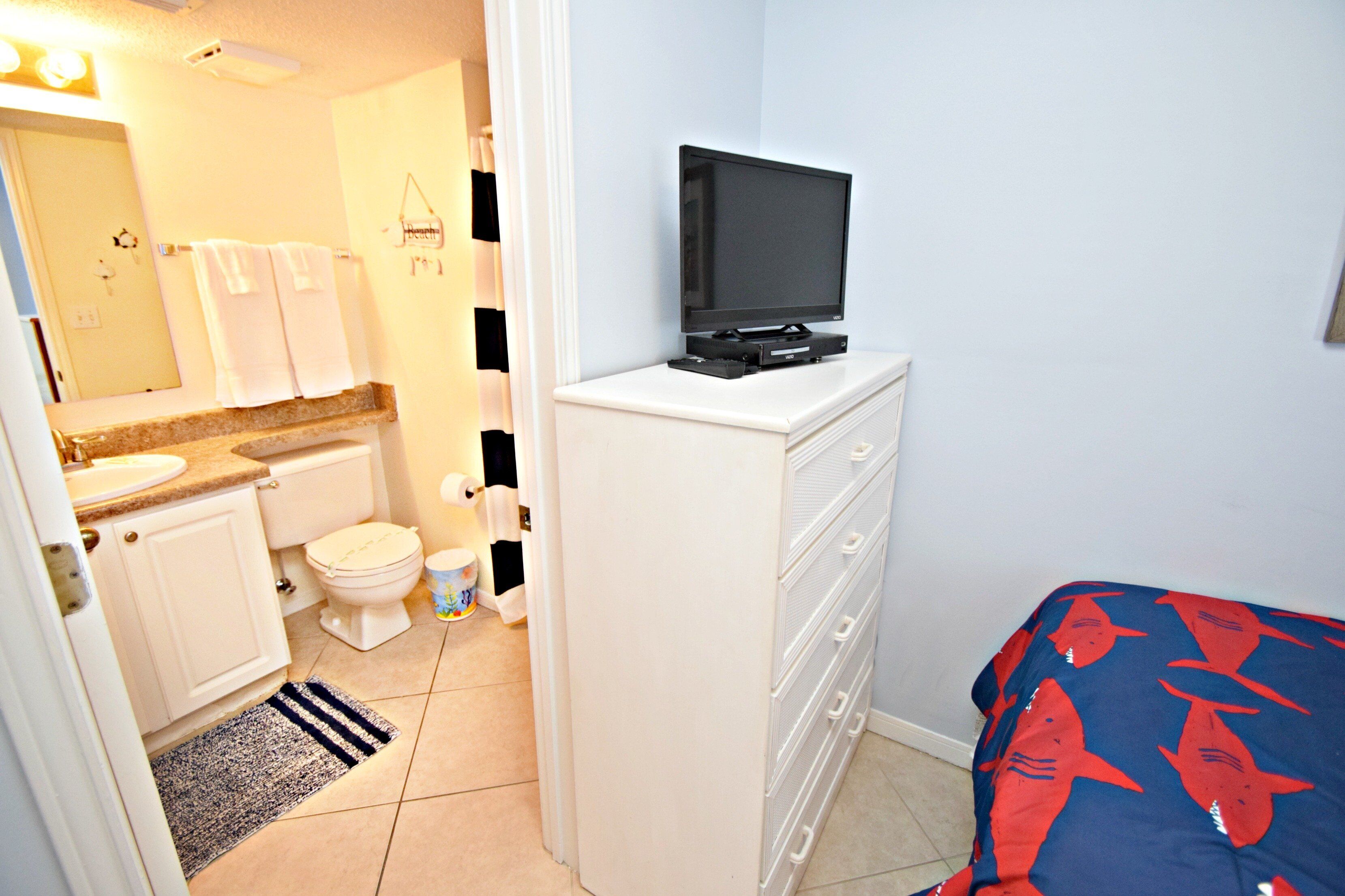 Une salle de bain équipée de toilettes, d’un lavabo et d’un téléviseur posé sur un meuble.
