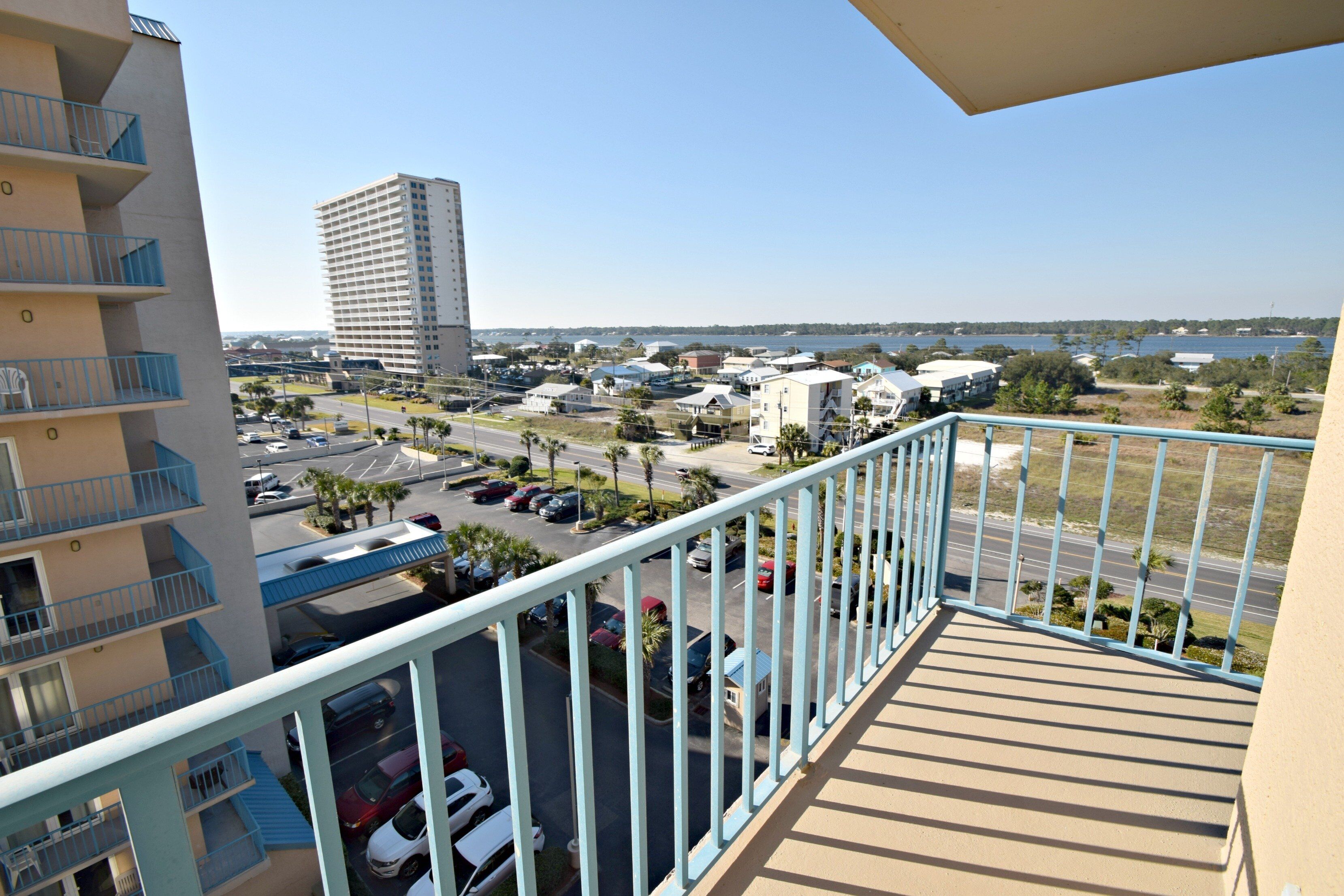 A balcony with a view of a parking lot, a tall building, and a body of water.