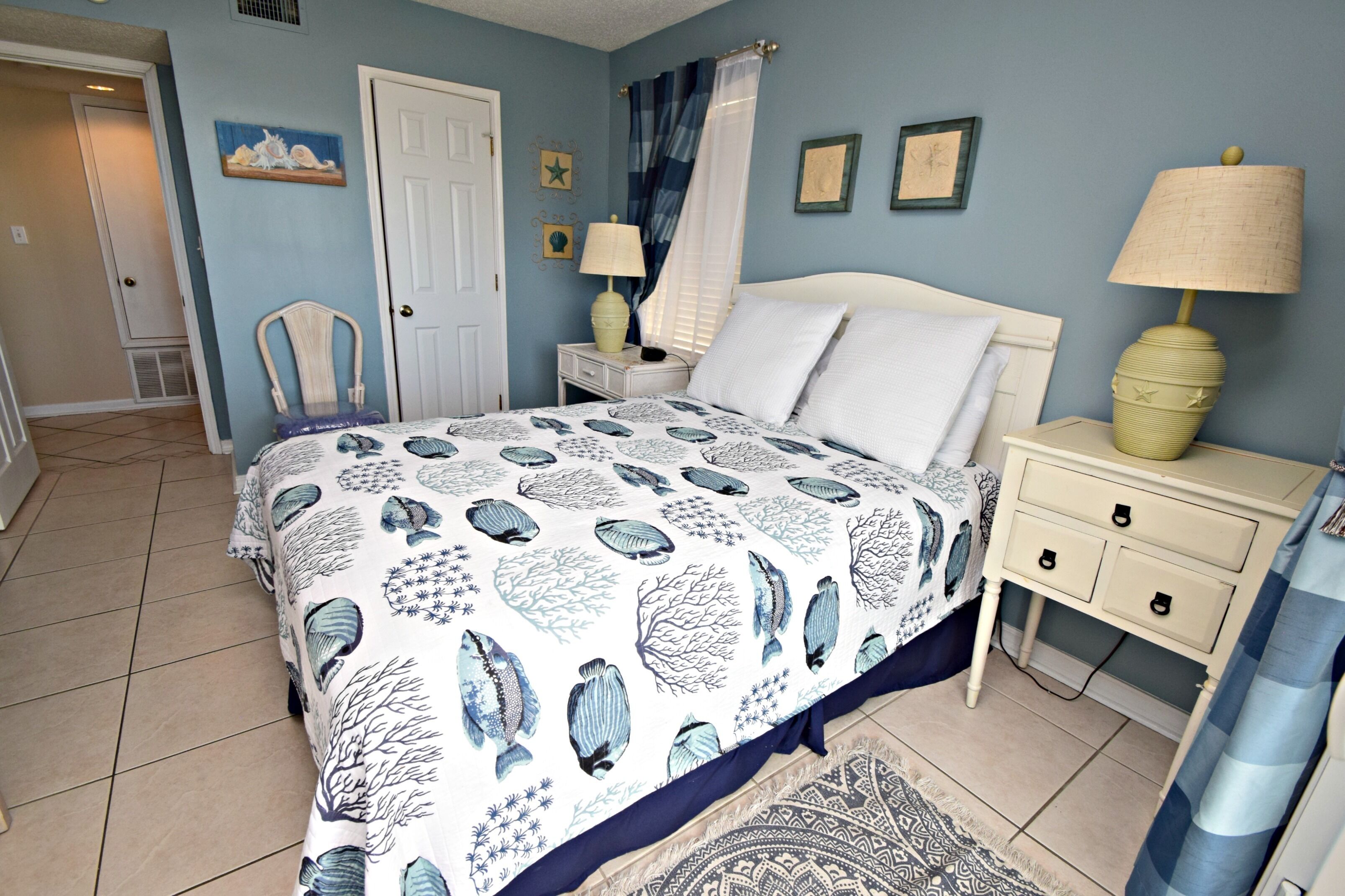 Un dormitorio con cama, mesitas de noche, una silla y una alfombra.