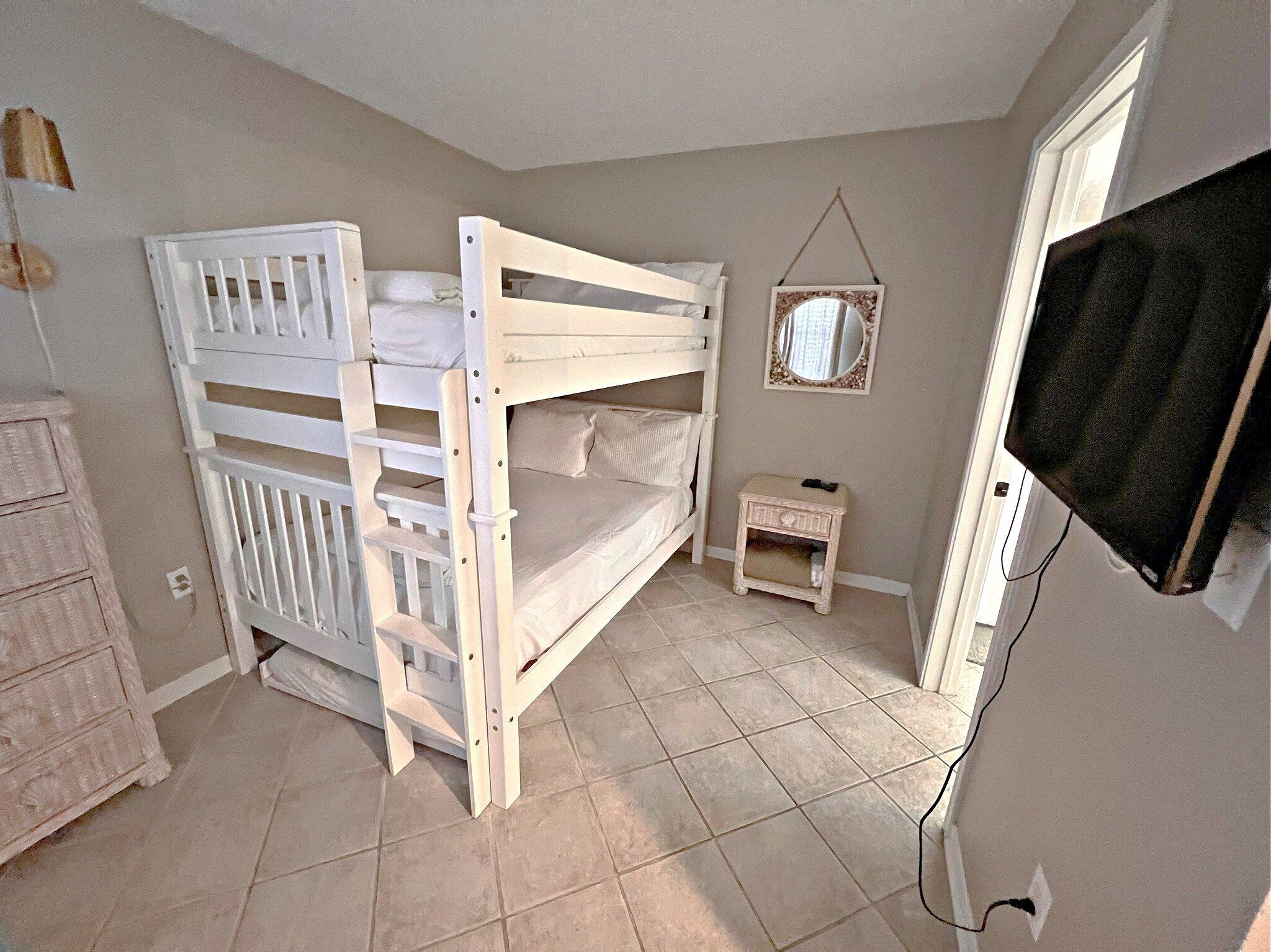 A bedroom with bunk beds, a small bedside table, a mirror, and a television.