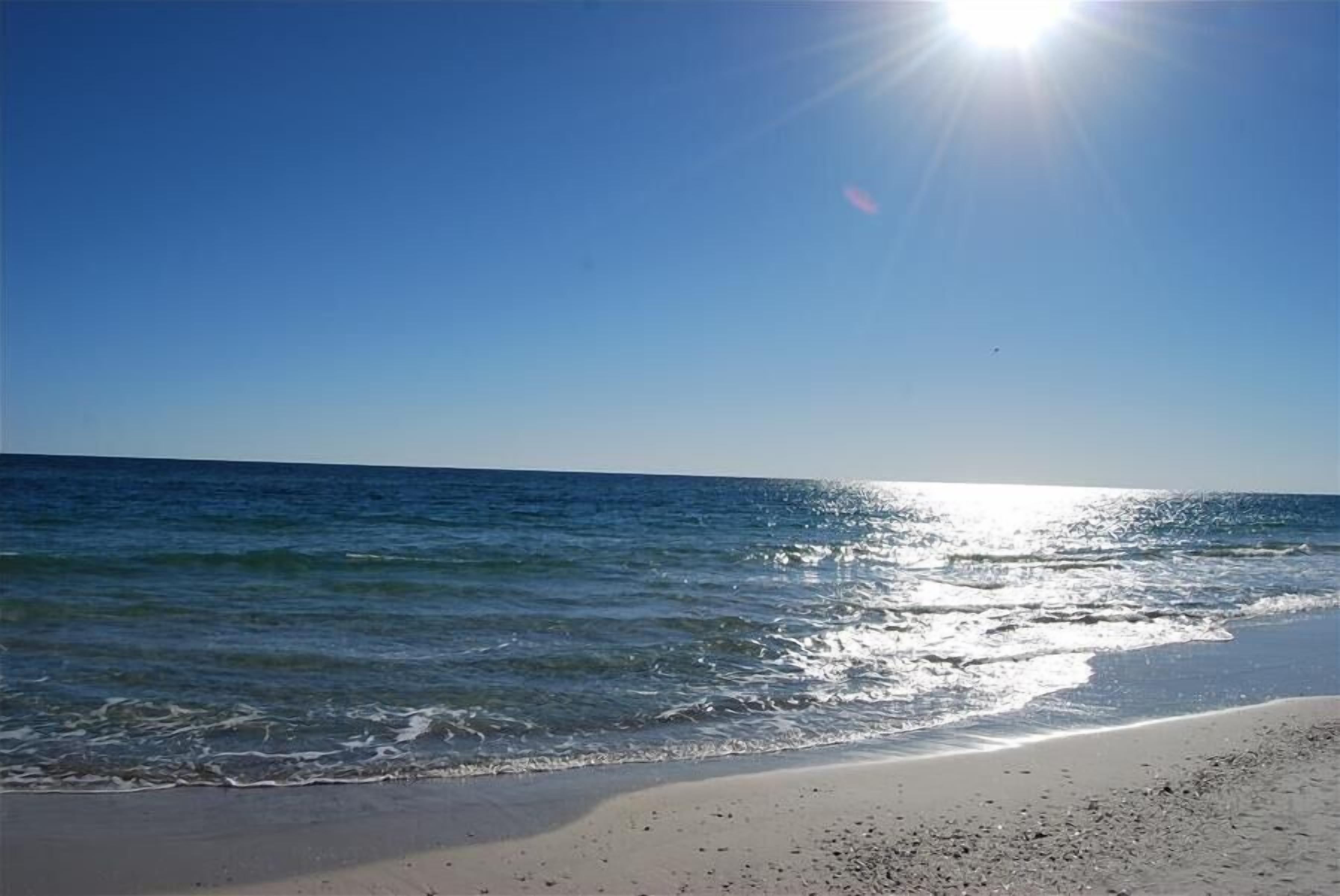 Una playa con cielos despejados y el agua brillando bajo el sol.