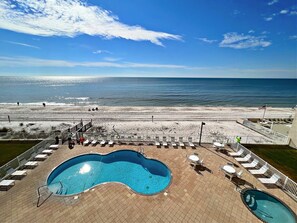 Un área de piscina con dos piscinas, una playa al fondo y un cielo despejado.