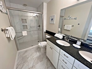 A modern bathroom with a glass-enclosed shower, a white toilet, a sink with a mirror, and a vanity with drawers. - The Indies (Gulf Shores)