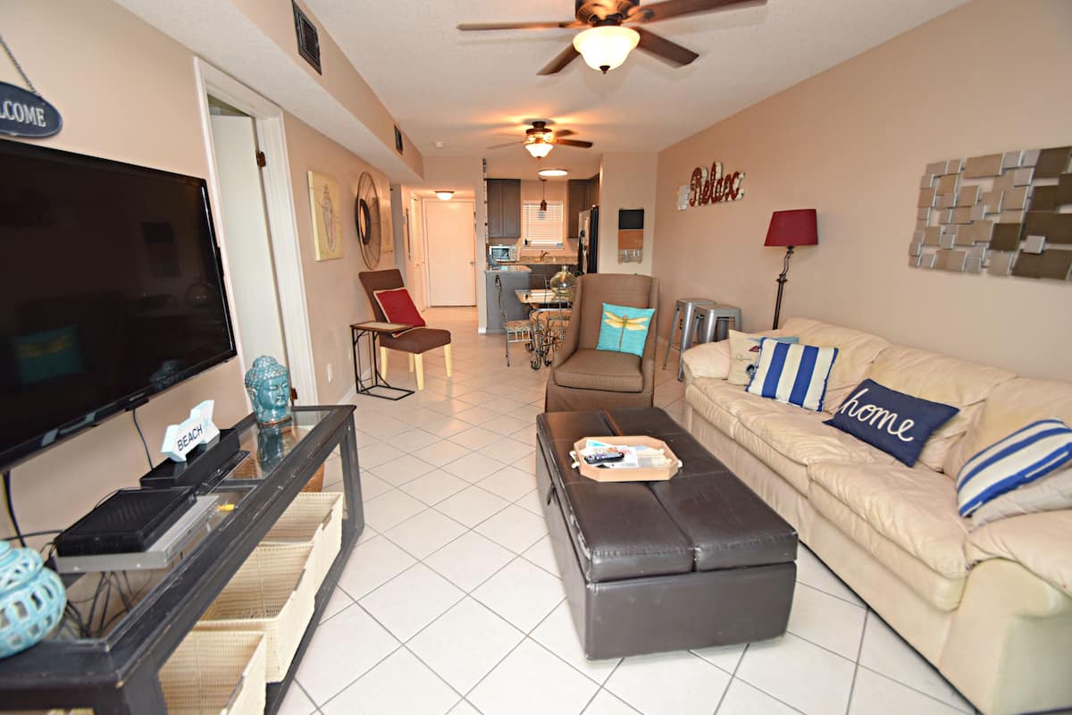 A living room with a television, a sofa, a coffee table, and a dining area in the background.