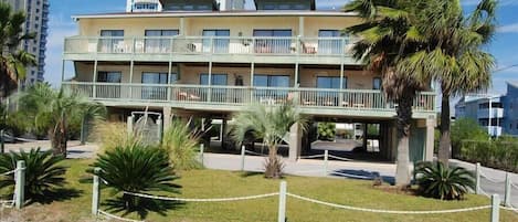 Un hôtel à plusieurs étages doté de balcons, entouré de palmiers et bordé d’une zone sablonneuse.
