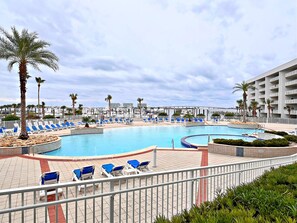 Zona de piscina en un resort con varias piscinas, palmeras y sillas de descanso.