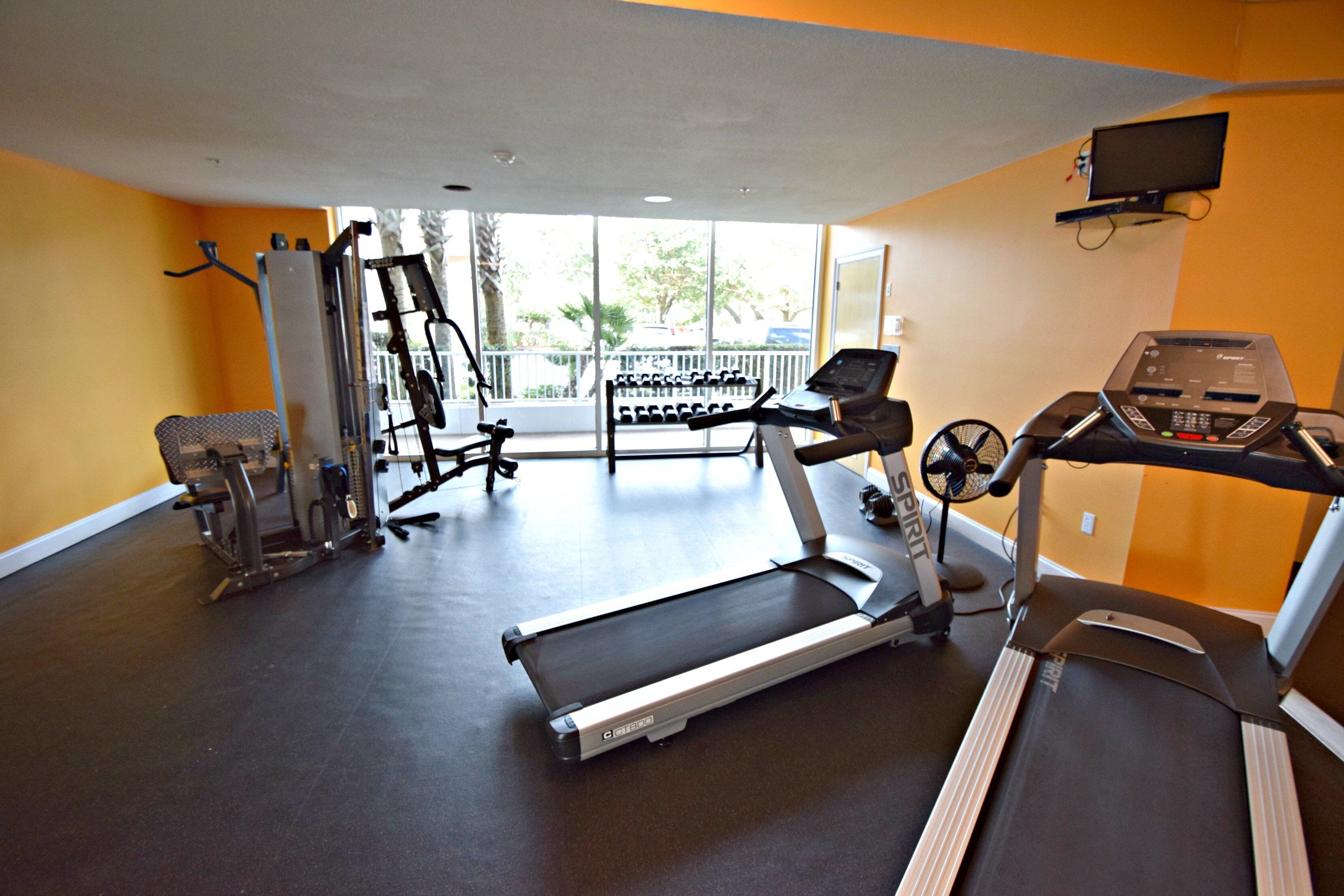 A gym with a treadmill, weight machines, and a bench.