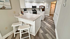 A modern kitchen with white cabinetry, a central island with stools, and a herringbone wood floor. - The Palms (Orange Beach)