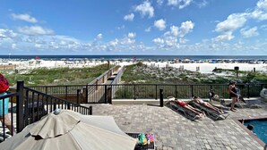 A beach view from a resort with a pool area, lounge chairs, and umbrellas. - The Palms (Orange Beach)