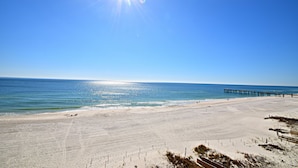 A beach with a pier extending into the ocean, clear skies, and a bright sun. - The Palms (Orange Beach)