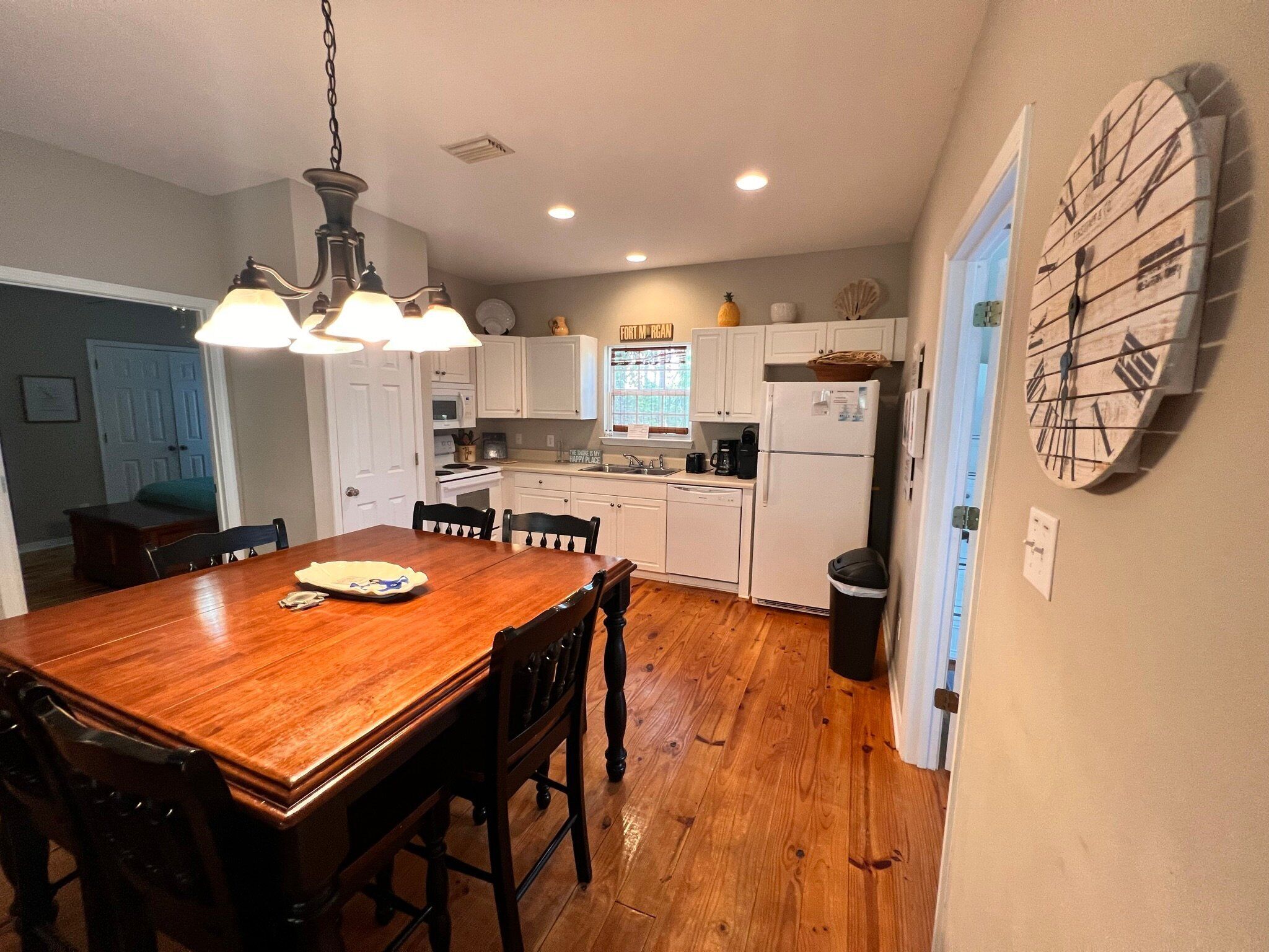 A kitchen with white cabinets, a wooden dining table, and a wall clock.