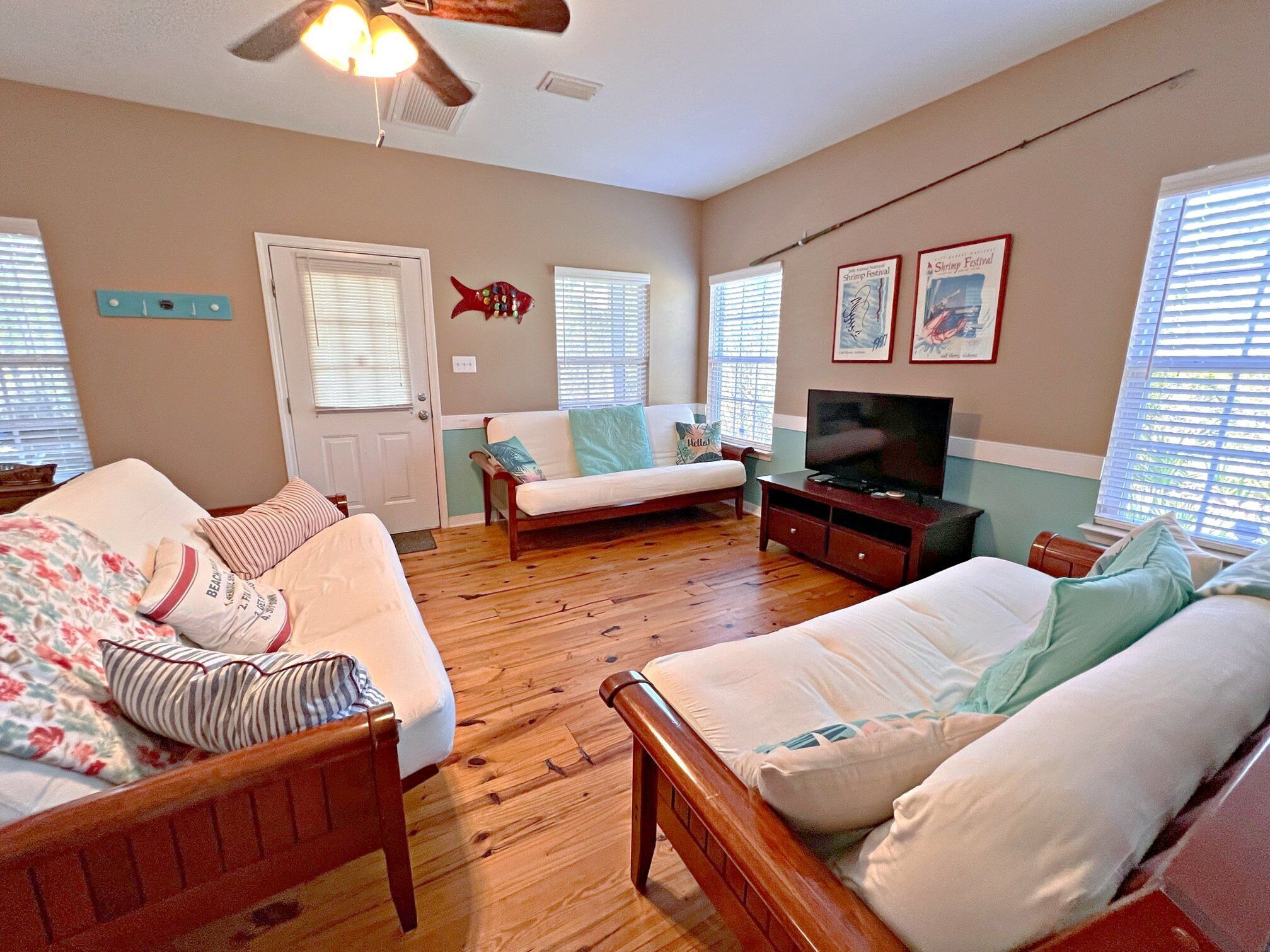 A cozy living room with a wooden floor, a sofa, a loveseat, a TV, and a ceiling fan.