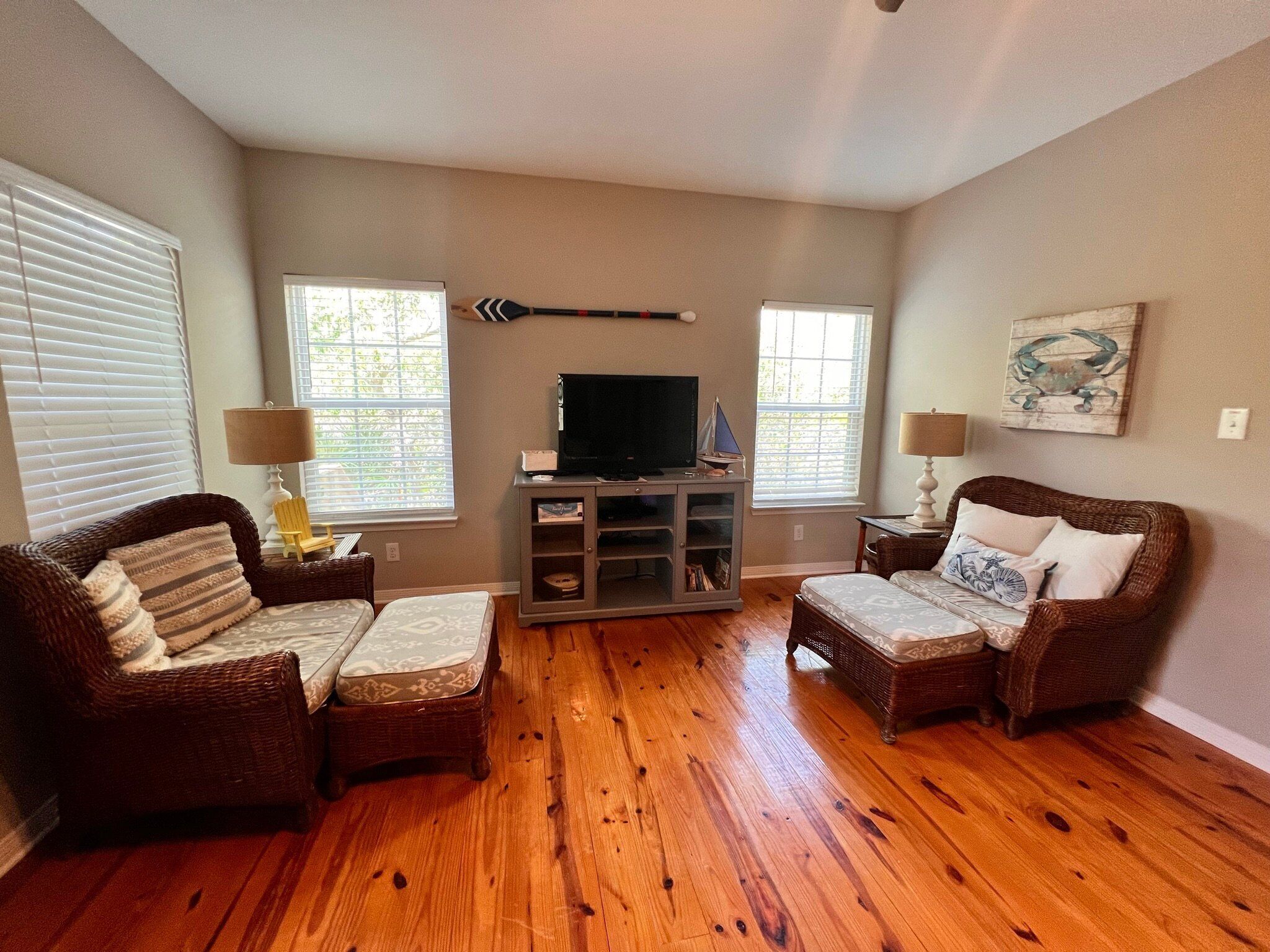 A living room with two wicker sofas, a television on a cabinet, and two windows with blinds.