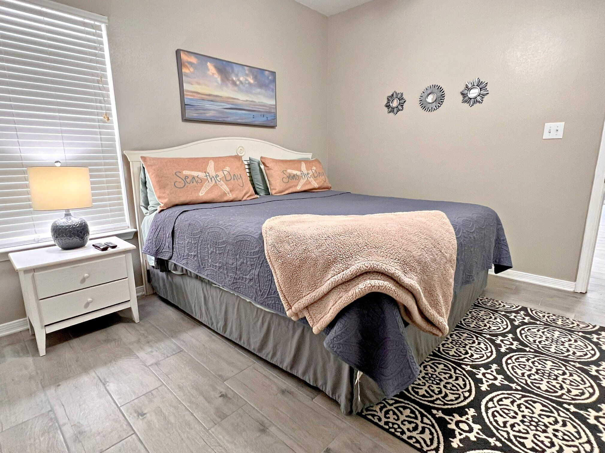 A bedroom with a bed, a nightstand, a lamp, a painting, and wall decor.