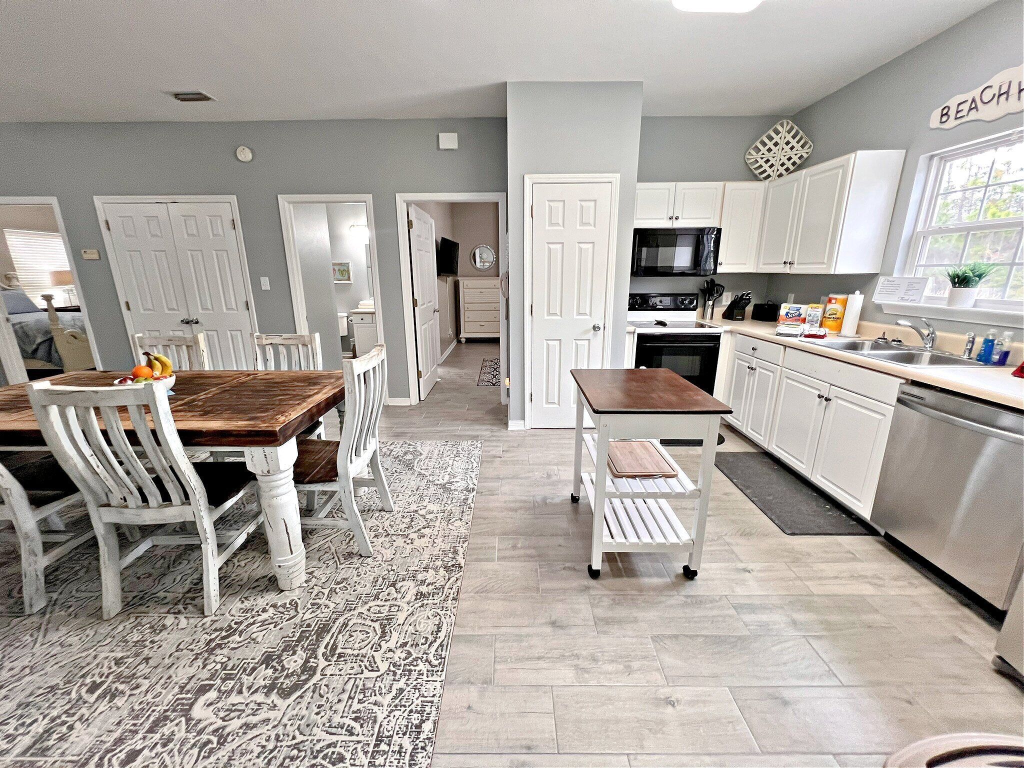 A modern kitchen with white cabinets, a wooden dining table, and a patterned rug.