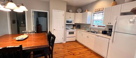 Una cocina con armarios blancos, una mesa de comedor de madera y un refrigerador.
