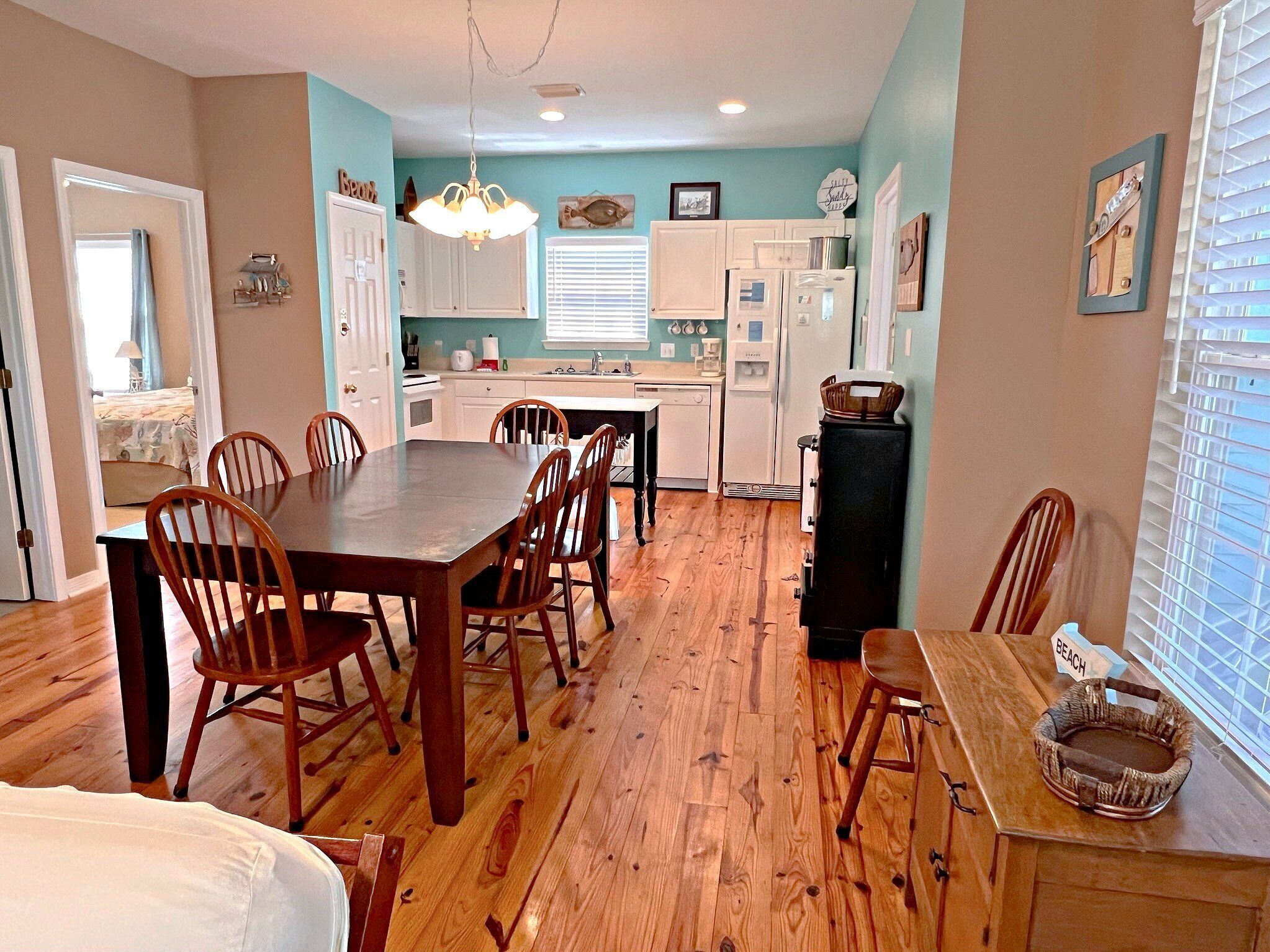 A spacious kitchen with wooden flooring, white cabinets, and a dining area with wooden chairs.