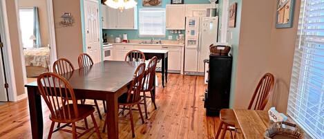 A spacious kitchen with wooden flooring, white cabinets, and a dining area with wooden chairs.