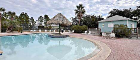 A swimming pool with lounge chairs and a thatched-roof structure.