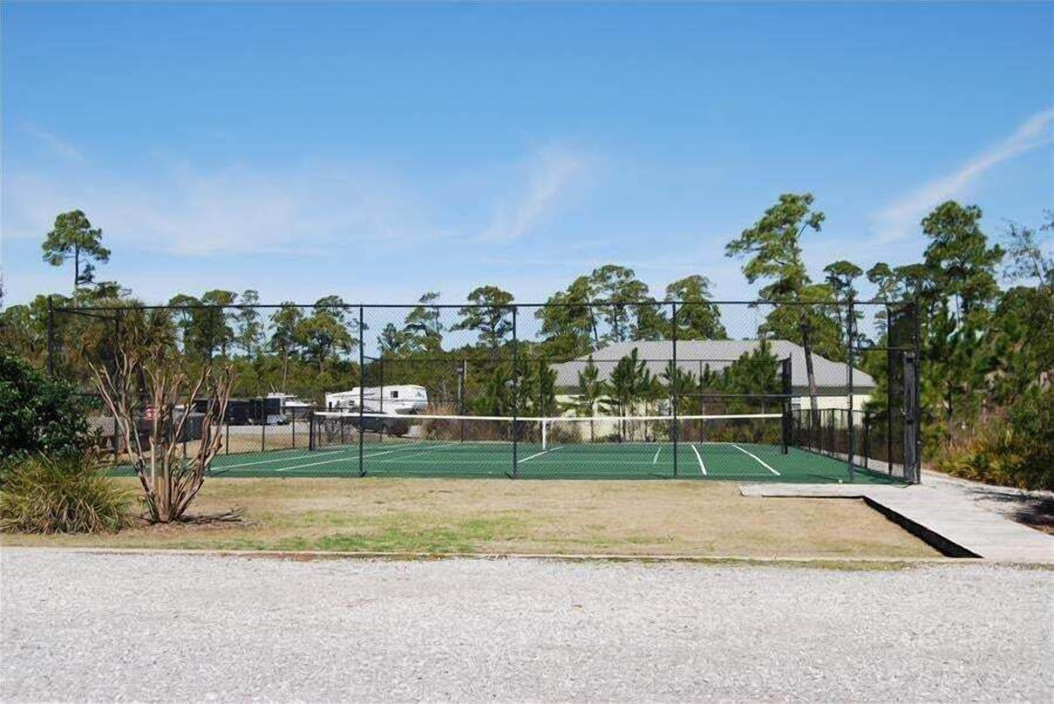 A tennis court with a fence, trees, and a building in the background.