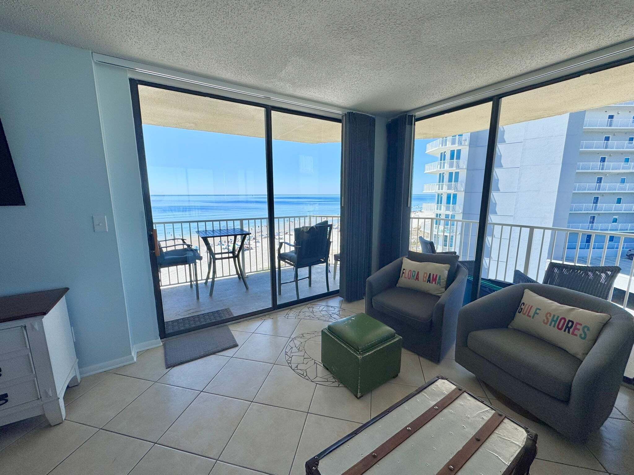 A balcony with a view of the beach and ocean, a sofa, a chair, and a small table.