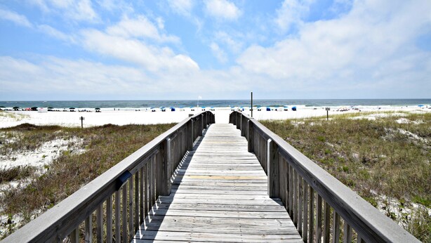 A wooden boardwalk leading to a beach with sand dunes and beach umbrellas. - Tidewater (Orange Beach)