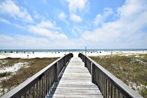A wooden boardwalk leading to a beach with sand dunes and beach umbrellas. - Tidewater (Orange Beach)