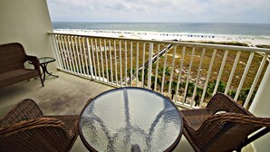 A balcony with wicker furniture, a glass table, and a view of the beach and ocean. - Tidewater (Orange Beach)
