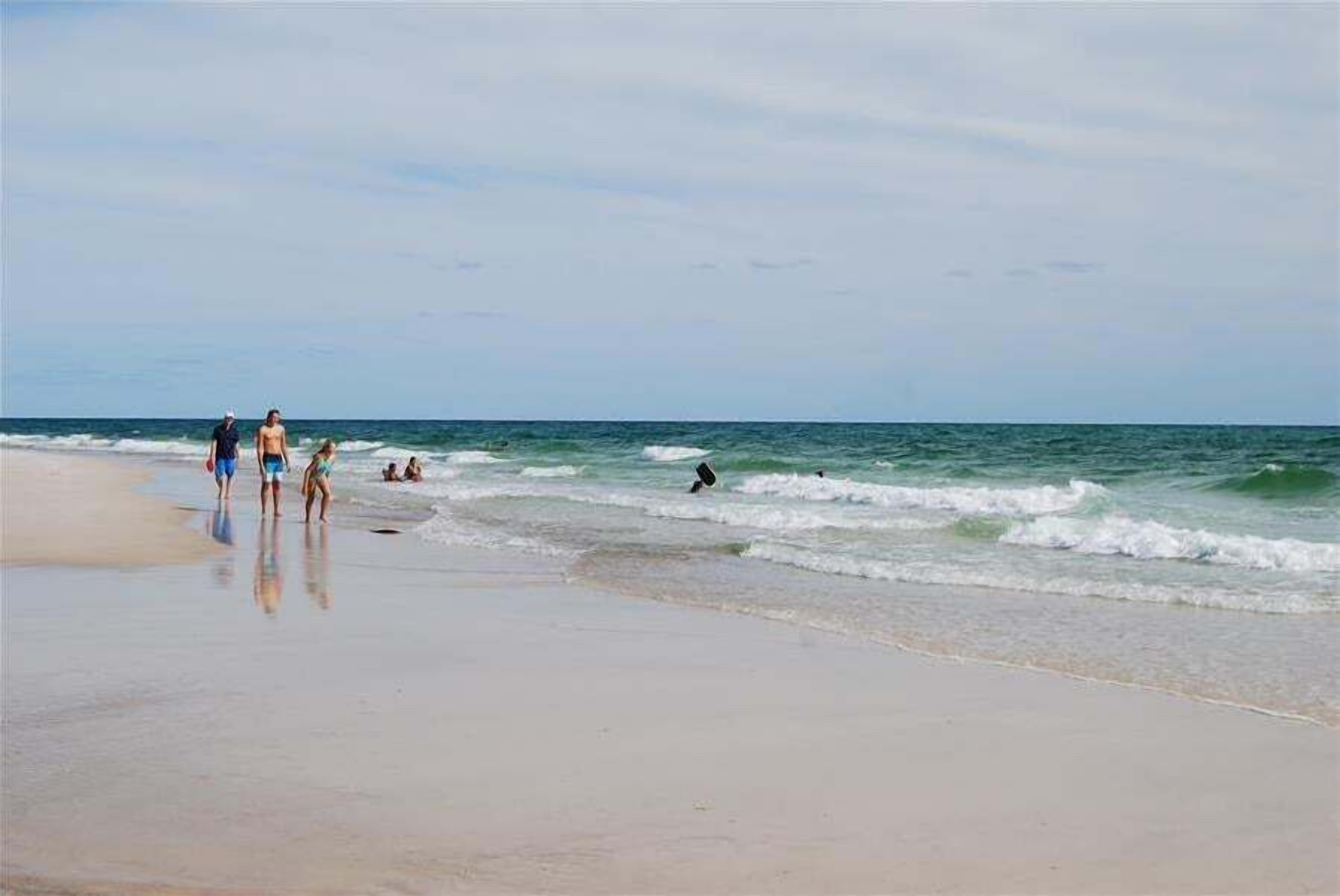 A beach with people walking and swimming.